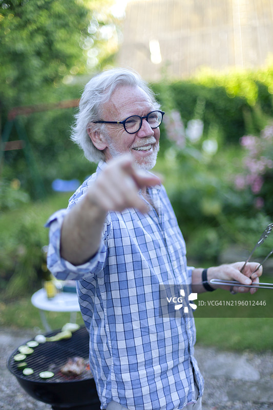 老年男子在后院准备烧烤时指着某处的肖像。图片素材