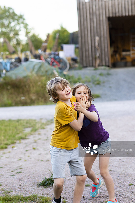 顽皮的哥哥在土路上捂住妹妹的嘴图片素材