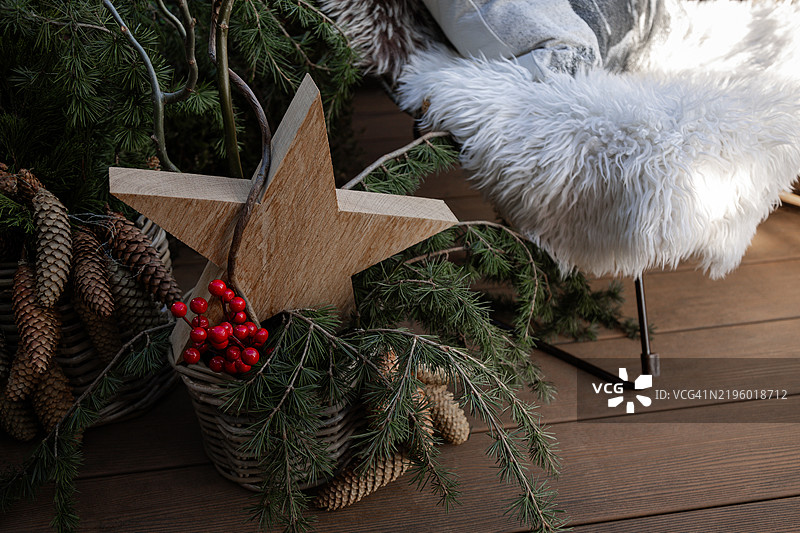 木制星星、带松果的云杉枝、浆果和植物放在椅子旁的篮子里，椅子上有毛茸茸的覆盖物。图片素材