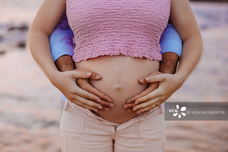 非常特写的孕妇肚子，温柔地被两只手轻轻托住。图片素材
