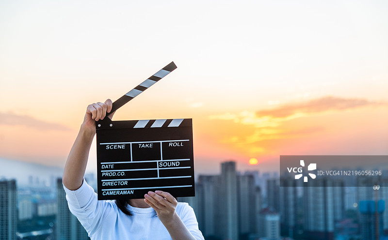 女人的手在日落天空的城市背景下握着电影拍板图片素材