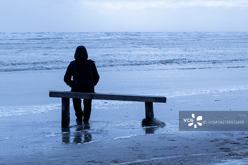 一个无法辨认的人坐在海滩上的长椅上图片素材