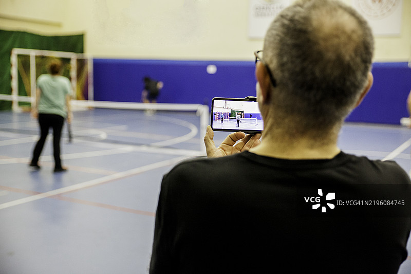 一个男人背对着镜头，用摄像机拍摄打腌黄瓜球的运动员们图片素材