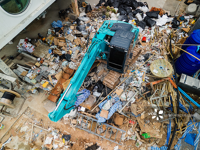 从空中俯瞰一台青绿色挖掘机在充满碎片、垃圾和废弃建筑材料的施工现场作业。图片素材