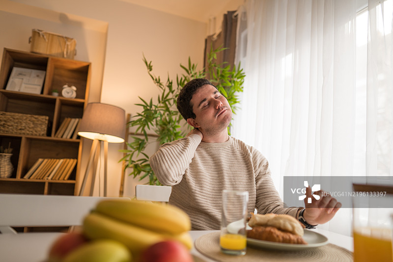 一个男人在早餐时感到脖子疼痛图片素材