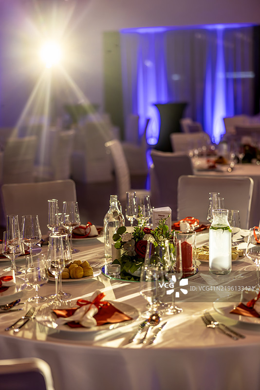 节日的情人节或婚礼桌面布置，配有白色餐盘、红色餐巾和玫瑰花。情人节或婚礼的桌面装饰，包含餐盘和酒杯。图片素材