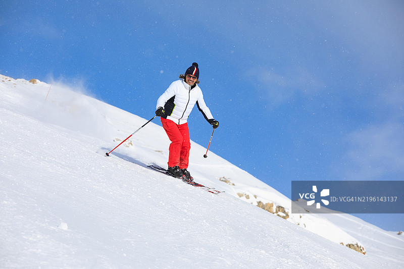 滑雪冬季运动，露出灿烂笑容的快乐。英俊的运动员在阳光明媚的滑雪胜地享受滑雪的乐趣。蓝天上飘落着大雪花。图片素材