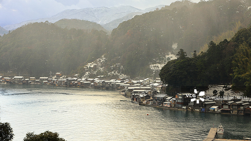 美丽的冬季景色，寒冷的冬季傍晚，雪花纷飞，夕阳西下，俯瞰伊根湾的伊根舟屋。图片素材
