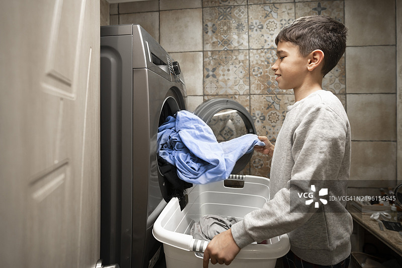 年轻男孩在洗衣机里装衣物，家庭环境中的家务活。图片素材