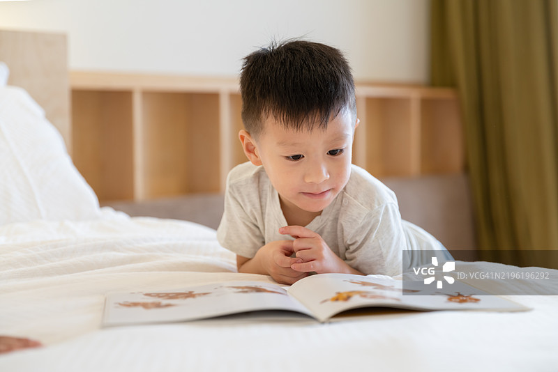 男孩躺在床上看图画书。图片素材