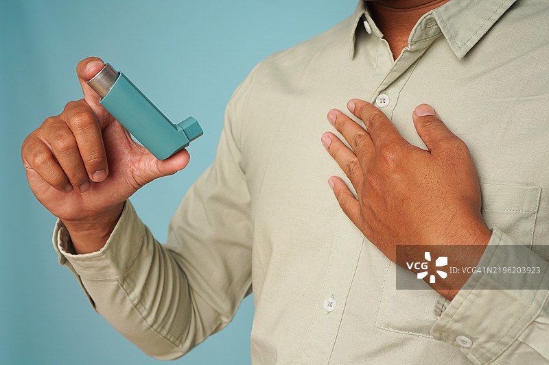 一名男子在蓝色背景下用气喘吁吁的姿势展示吸入器图片素材
