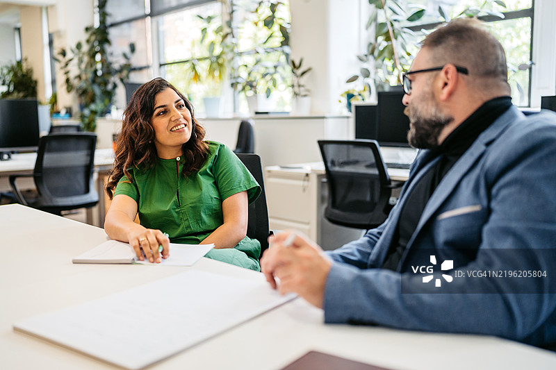 两位中年同事在澳大利亚悉尼的办公室桌前交谈图片素材