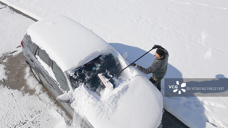 男子在北卡罗来纳州格林维尔为SUV挡风玻璃清除雪花 - 高角度拍摄图片素材