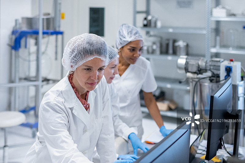 一群女性药剂师在制药实验室的电脑后工作，生产化妆品。图片素材
