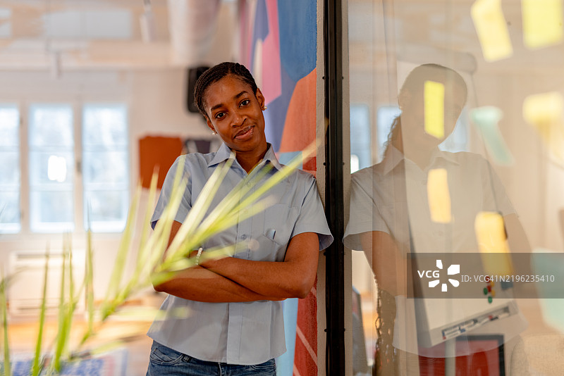 年轻的黑人女商人在现代办公室微笑，双臂交叉。图片素材