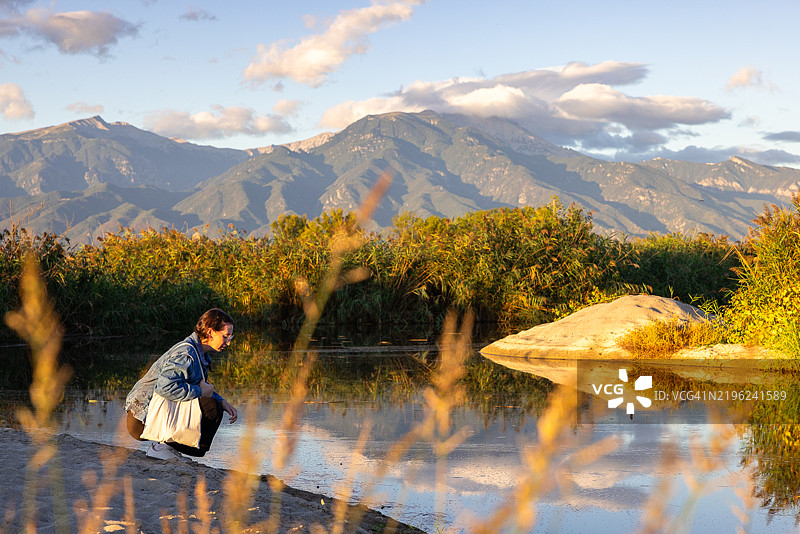 一位女性在希腊的河口沿岸晨跑，背景是奥林匹斯山。图片素材