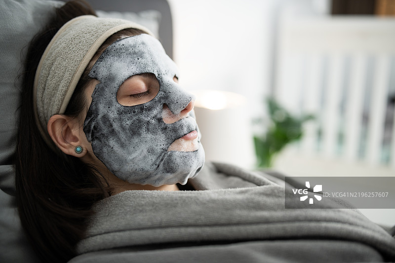 年轻女性在家中放松，脸上贴着面膜。图片素材