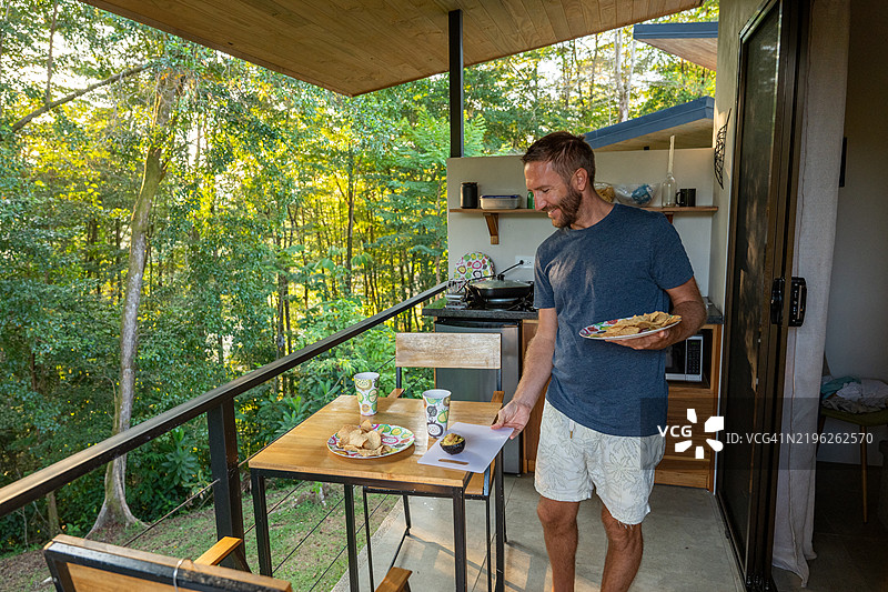 男子在阳台上享用森林景观的早餐图片素材