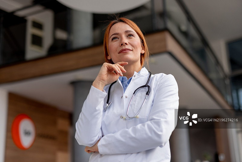 自信的女性医生在现代医疗设施中思考，手持听诊器图片素材