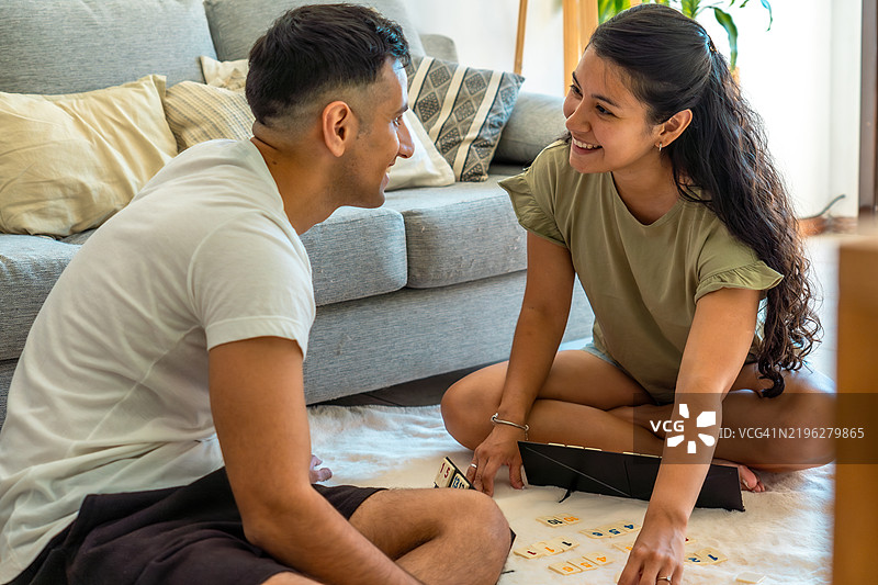 年轻的西班牙裔情侣在家里玩拉米牌，享受乐趣图片素材