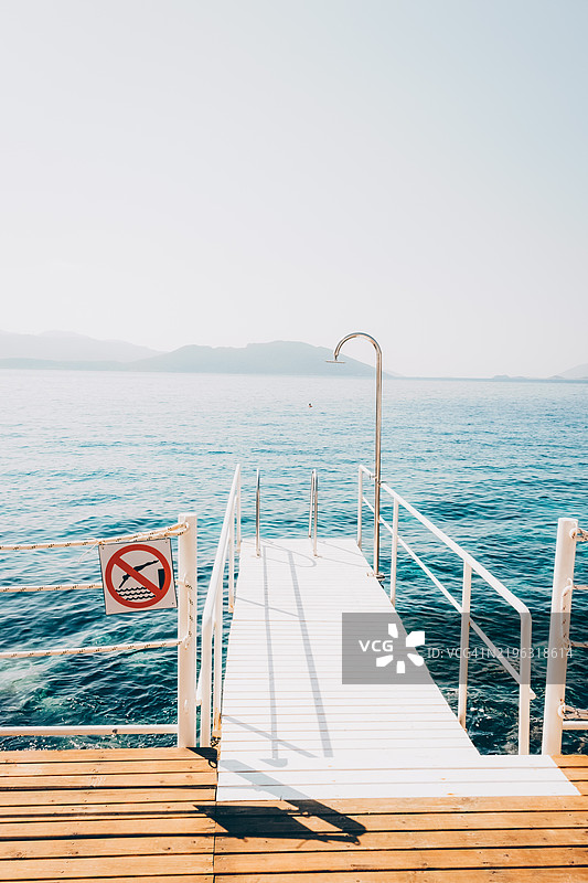 宁静的海岸码头，背景是平静的海洋，适合夏季度假设计。禁止潜水标志。码头海滩风景中的禁止潜水标志，假期和旅行背景概念。图片素材