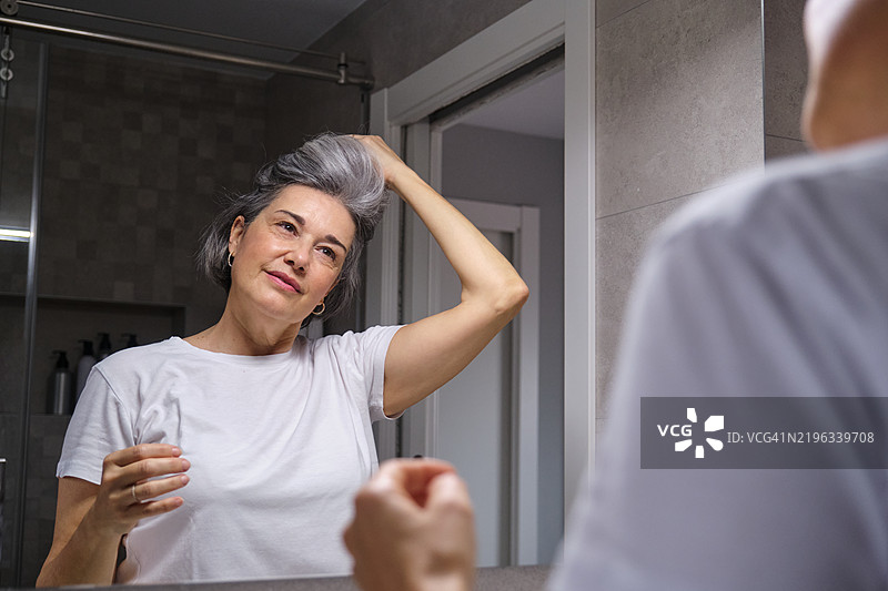一位年长女性在浴室镜子前梳理她的灰发图片素材