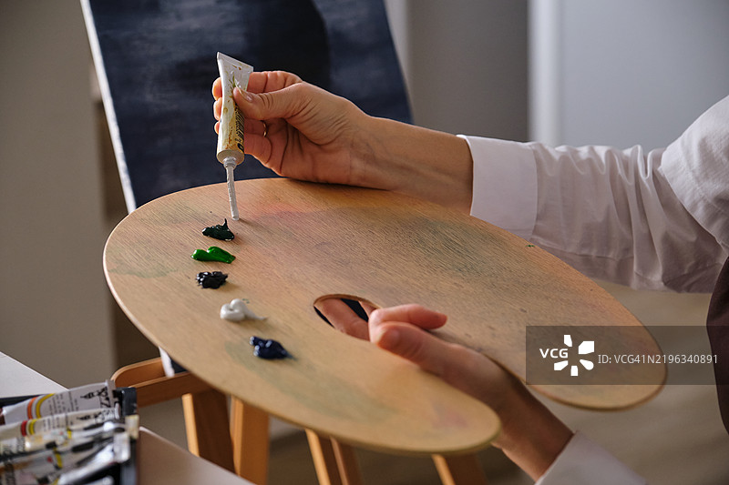 艺术家将白色颜料从管子挤到木质调色板上图片素材