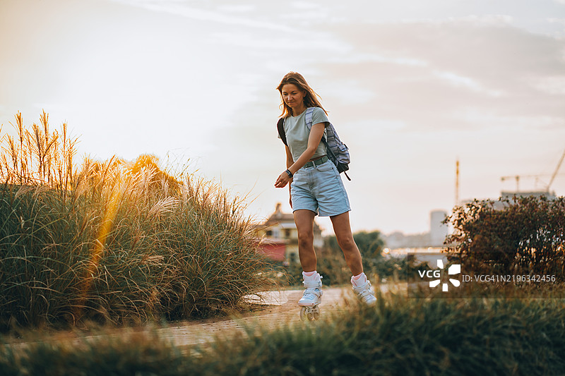 年轻女性在公园里日落时滑旱冰图片素材