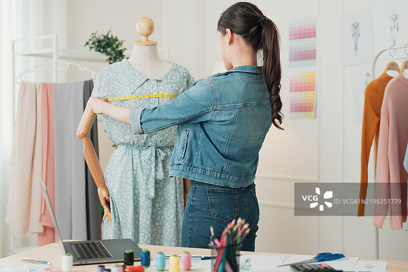 时尚设计师在创意设计工作室中为模特测量一件裙子图片素材