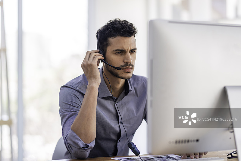 男性客服代表在办公室工作站佩戴耳机工作图片素材