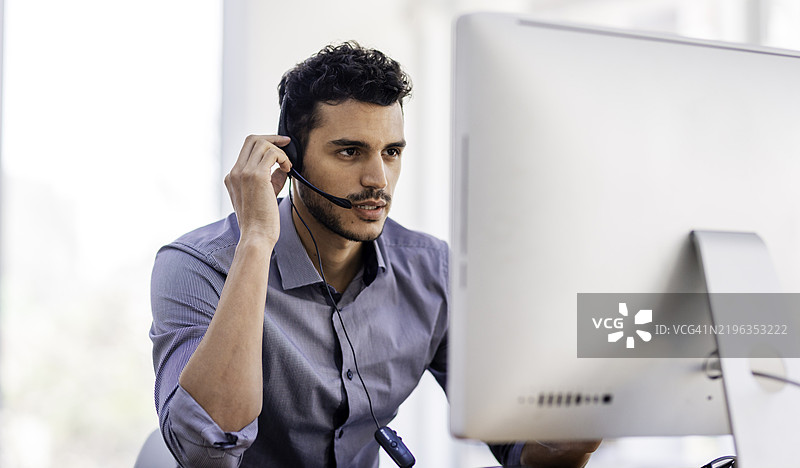 专业男性客服代表在电脑前认真工作，佩戴耳机。图片素材