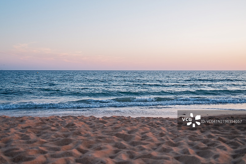 柔和的日落色彩映照在沙滩和宁静的海洋上图片素材