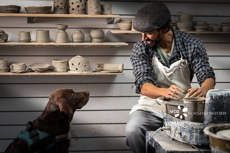 男人在制作陶器，狗狗在旁观看图片素材