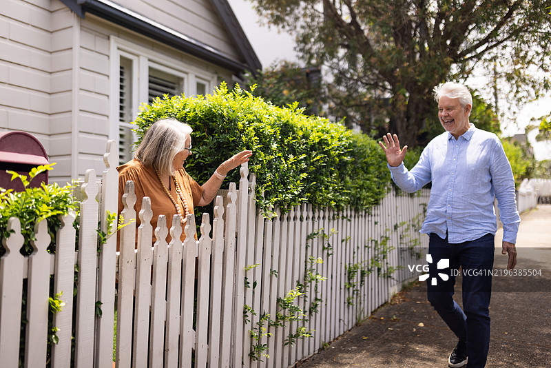 友好的邻居在阳光明媚的日子里通过白色栅栏打招呼图片素材