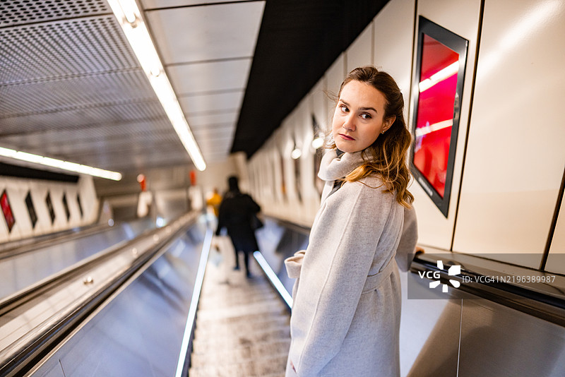 美丽的女人在自动扶梯上走下。图片素材