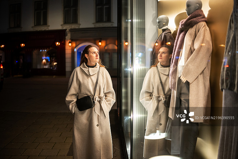 穿着外套的女人在服装店橱窗前漫步图片素材