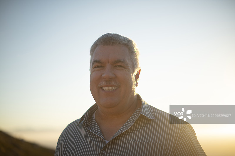夕阳下微笑的成熟男性肖像，旅行假期与户外冒险。自然保护，公园护林员，充满自信的快乐人在山丘上，傍晚的天空与生态旅游。图片素材
