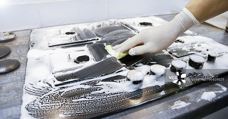 戴手套的手用清洁海绵擦拭厨房区域的肥皂灶台图片素材