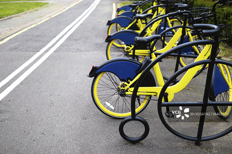 明亮的黄色自行车整齐地停放在城市环境中铺砌的小路旁的自行车架上图片素材