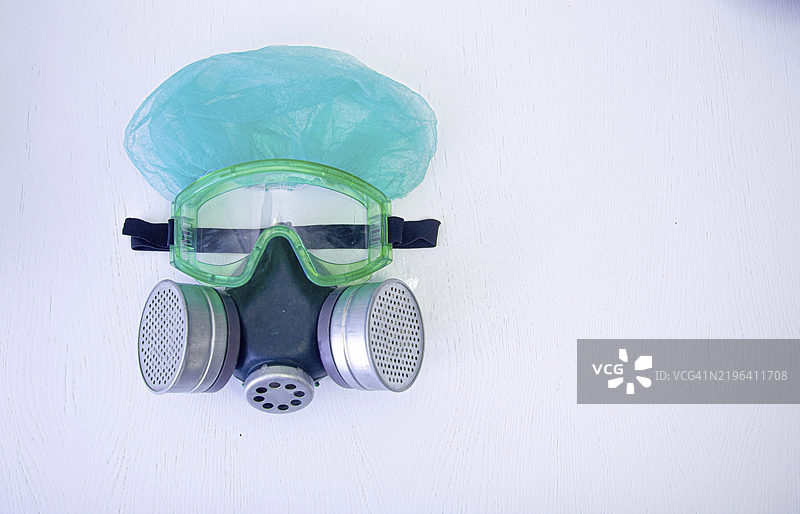 绿色护目镜和带蓝色帽子的双重过滤口罩放在白色表面上图片素材