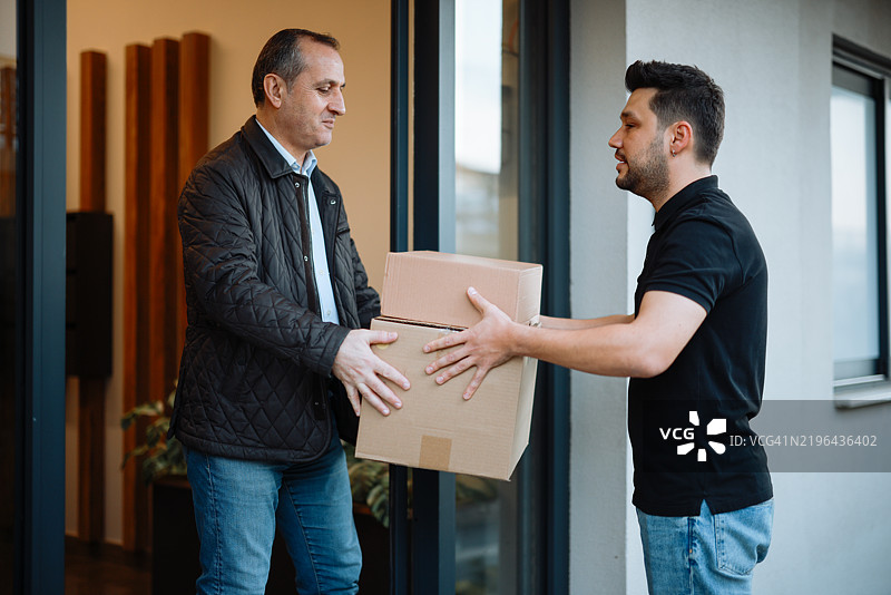 货运工作人员将装有包裹的纸箱递交给收件人的手部特写。图片素材