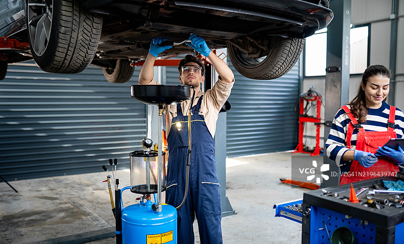 一名机械师在修理店里站在汽车下方排放发动机油。图片素材