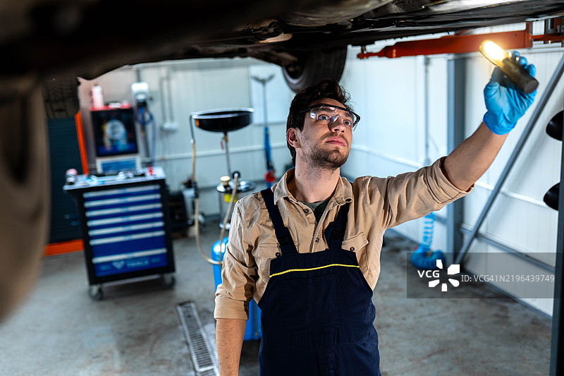汽车修理工在修理店用手电筒检查汽车底盘图片素材