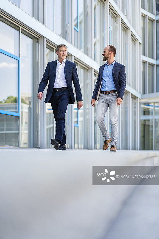 两位经理在现代建筑中散步，讨论业务。图片素材