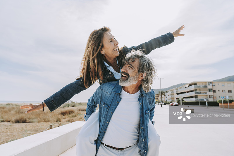 快乐的老年男子背着无忧无虑的女性去海滩图片素材