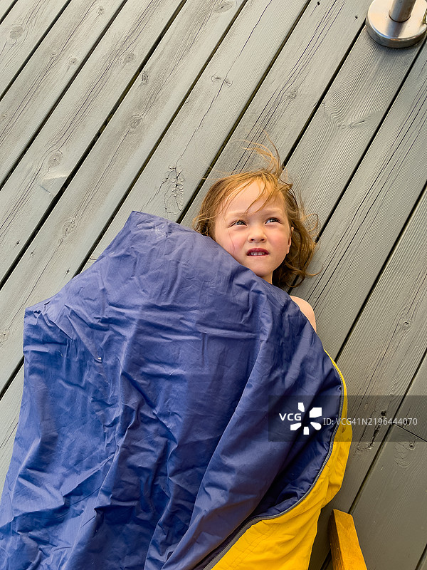 一个孩子躺在木甲板上，裹着睡袋。图片素材
