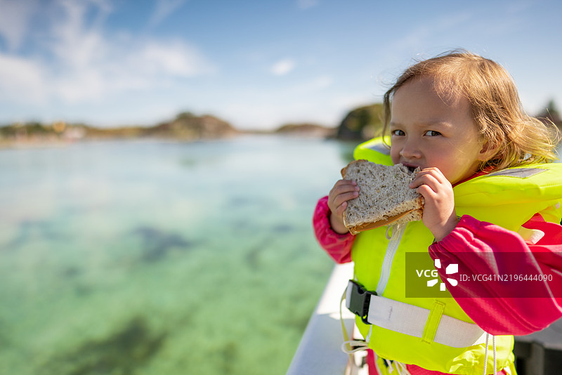 一个孩子在挪威奥斯特海姆的船上享受三明治。图片素材