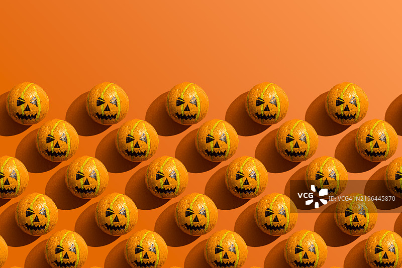 万圣节糖果的排成行的图案，外包装是南瓜灯，背景为橙色。图片素材