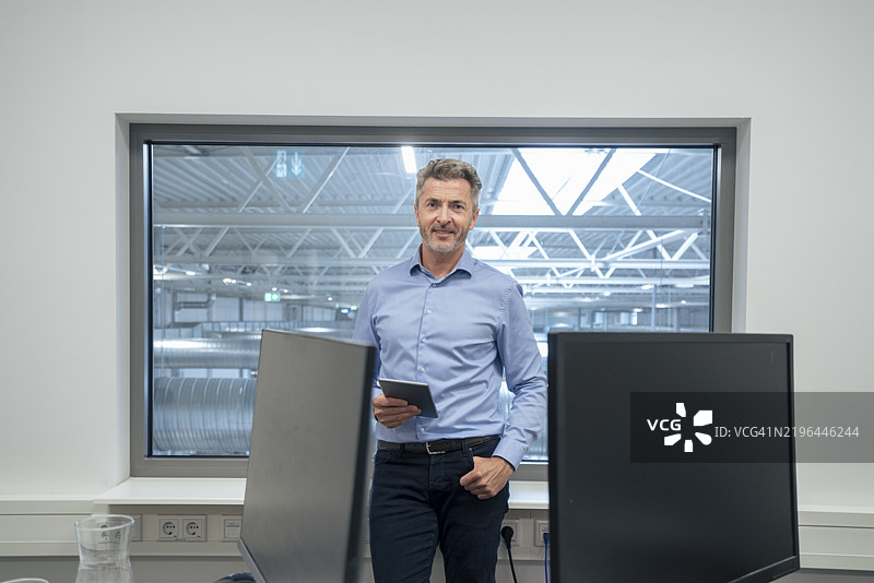 在办公室小隔间里，口袋里插着手的商人手持平板电脑。图片素材