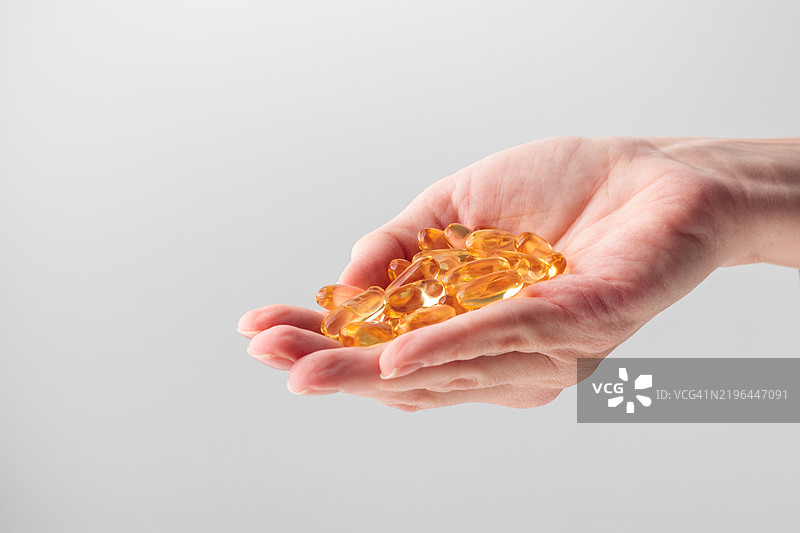 手握一把黄色的Omega 3或D维生素胶囊，背景为白色。鱼油黄色药丸，有助于预防心脏病和缺血性中风，护肤，抑郁症治疗。图片素材